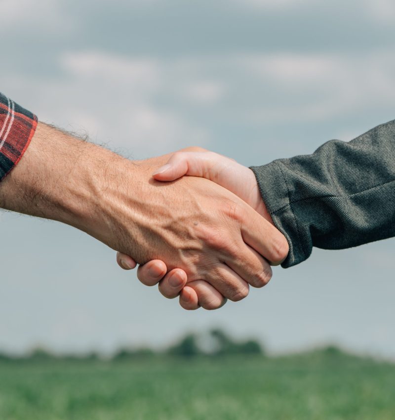 Mortgage loan officer and farmer shaking hands upon reaching an agreement for financial allowance application, banker and farm worker in corn maize crop field.